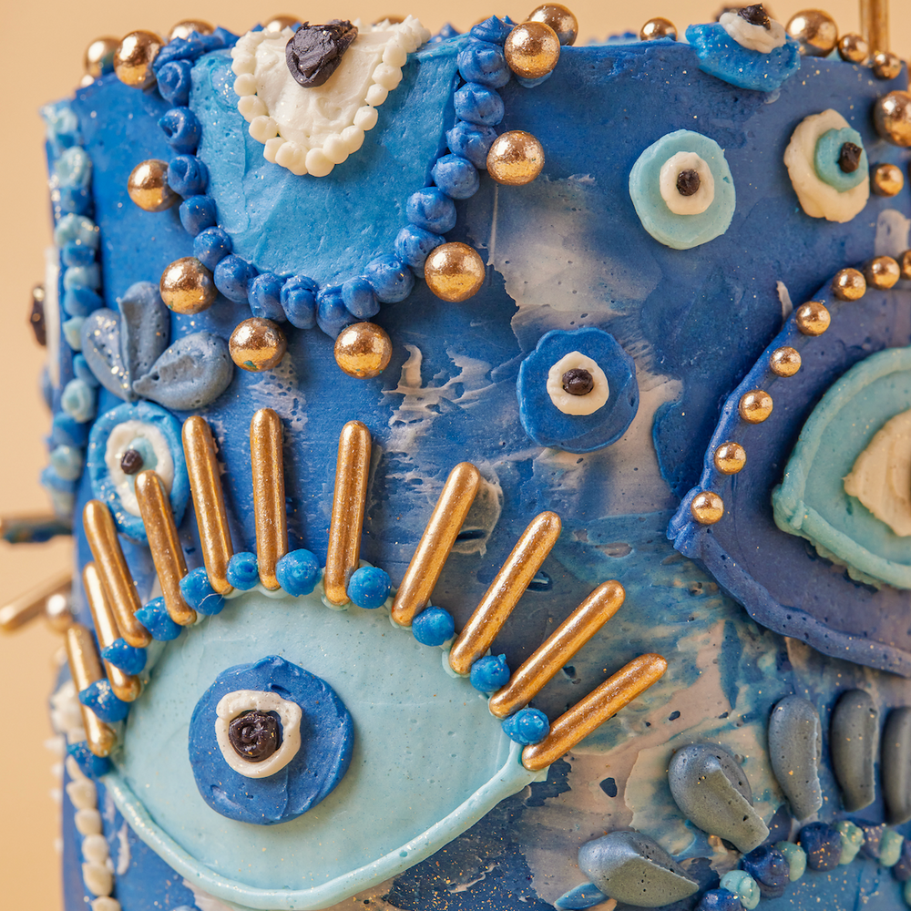 Decorative blue cake with intricate designs and gold accents on a beige background