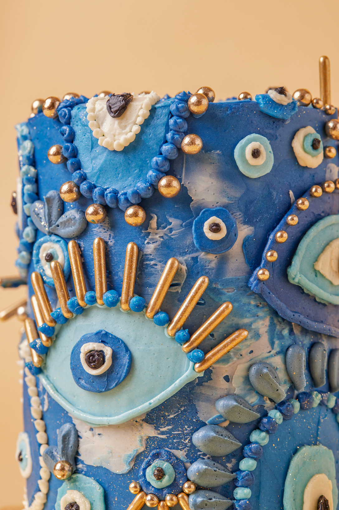 Decorative blue cake with intricate designs and gold accents on a beige background